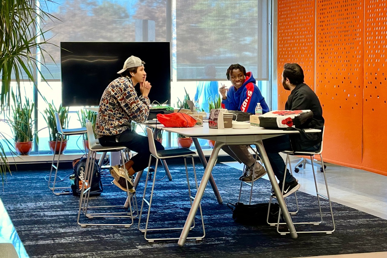Three students sit at a table in UC's 1819 Innovation Hub.