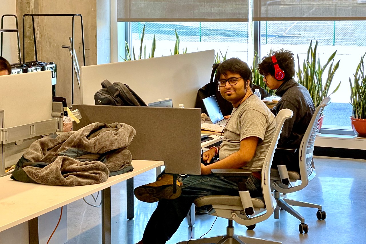 A male student sits at a table with laptop in UC's 1819 iHub.