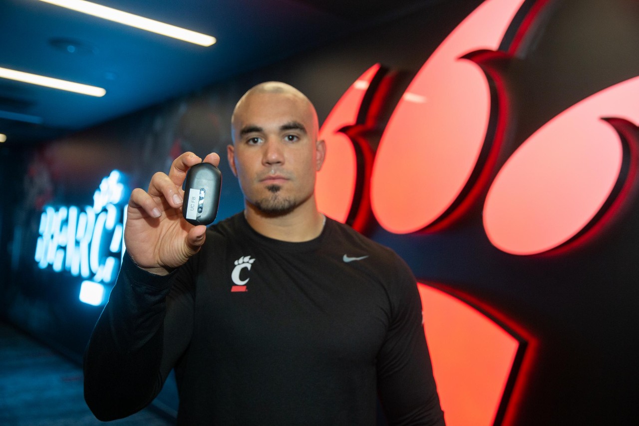 Assistant Director of Football Sports Performance Brandon Garcia holds up wearable technology that helps monitor player performance.