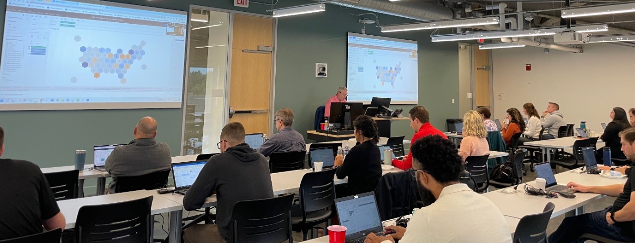 A man gives a presentation while students at a table look on.