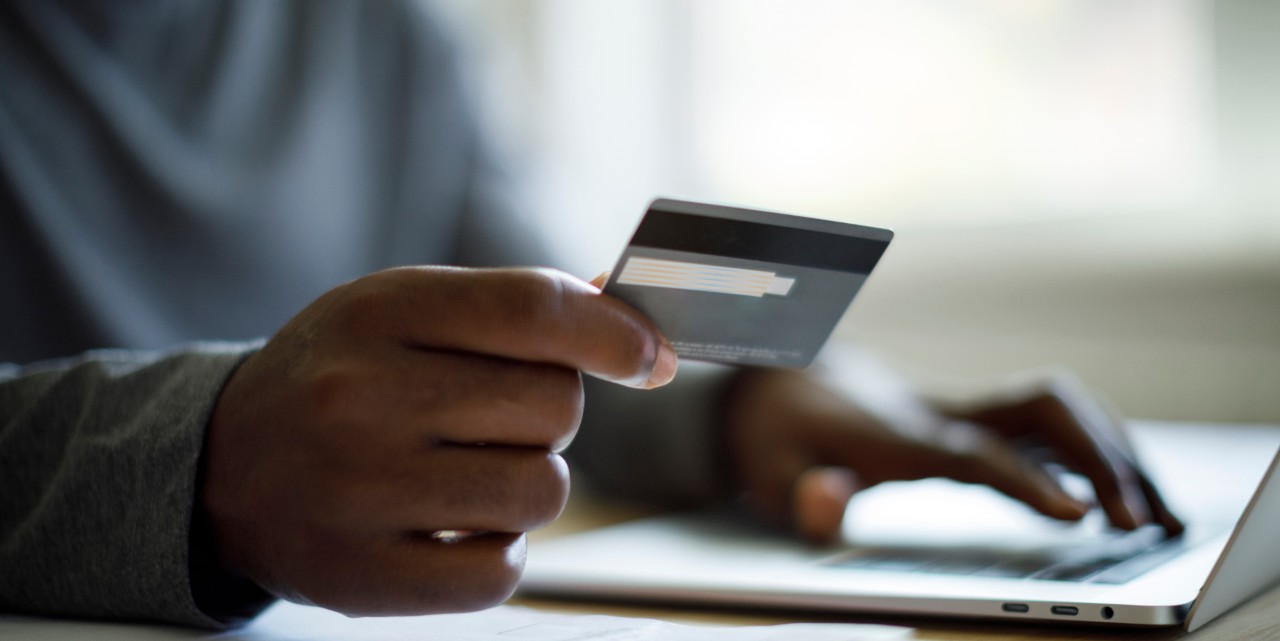 man holding a credit card in his hand while online shopping on the laptop