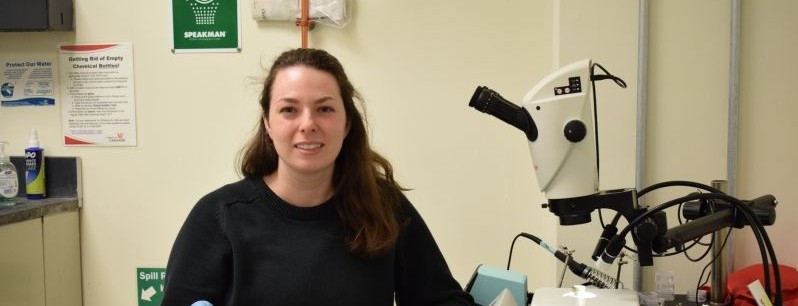 Eleanor Scott poses in a lab next to a microscope. 