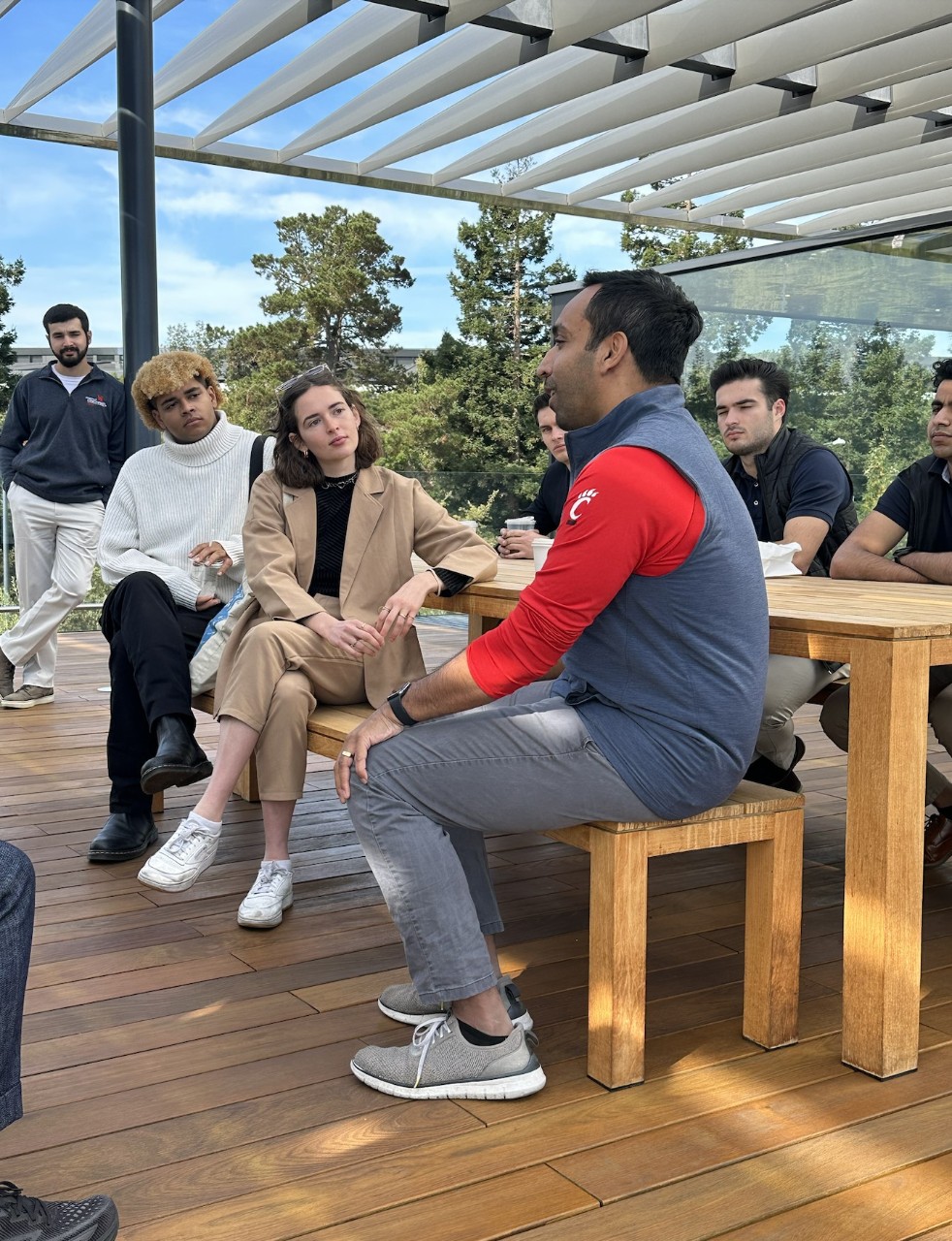 A seated man speaks to a group of students gathered around him.