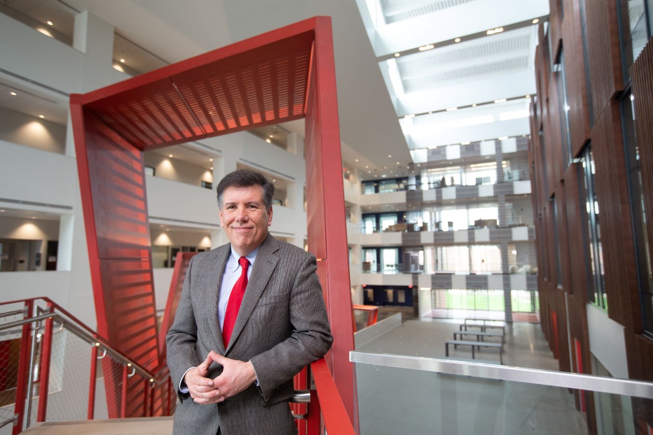 David Niven standing by a handrail in Clifton Court Hall. Niven is wearing a grey suit and red tie. 