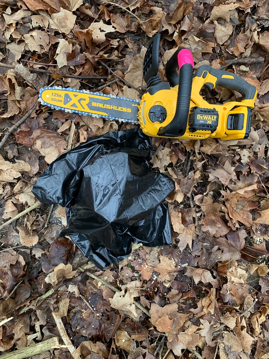 A chainsaw sits next to a stump wrapped in black plastic.