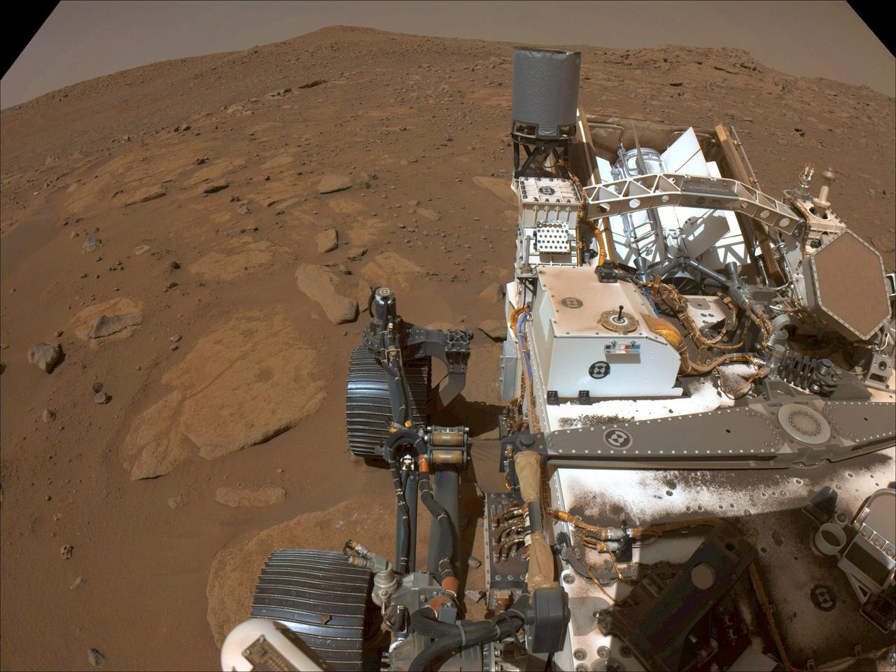 A slightly elevated view looking back across the top of the rover as it sits parked on the sandy surface of Mars.