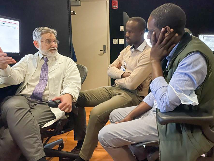 Harris, Niyigena and Muvunyi sit in front of a monitor; Harris is turned toward the other two and is gesturing as he speaks.