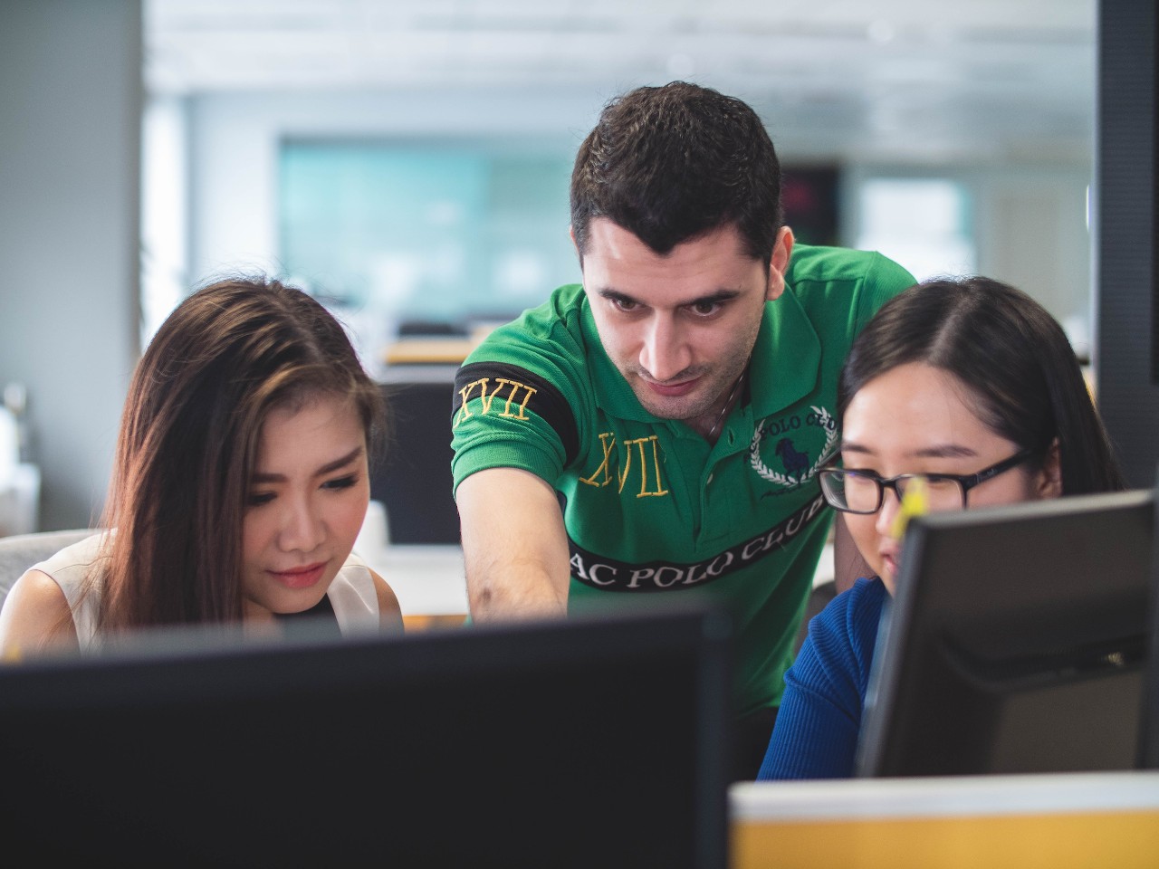 Two women and a man stand over two laptops facing the viewer.