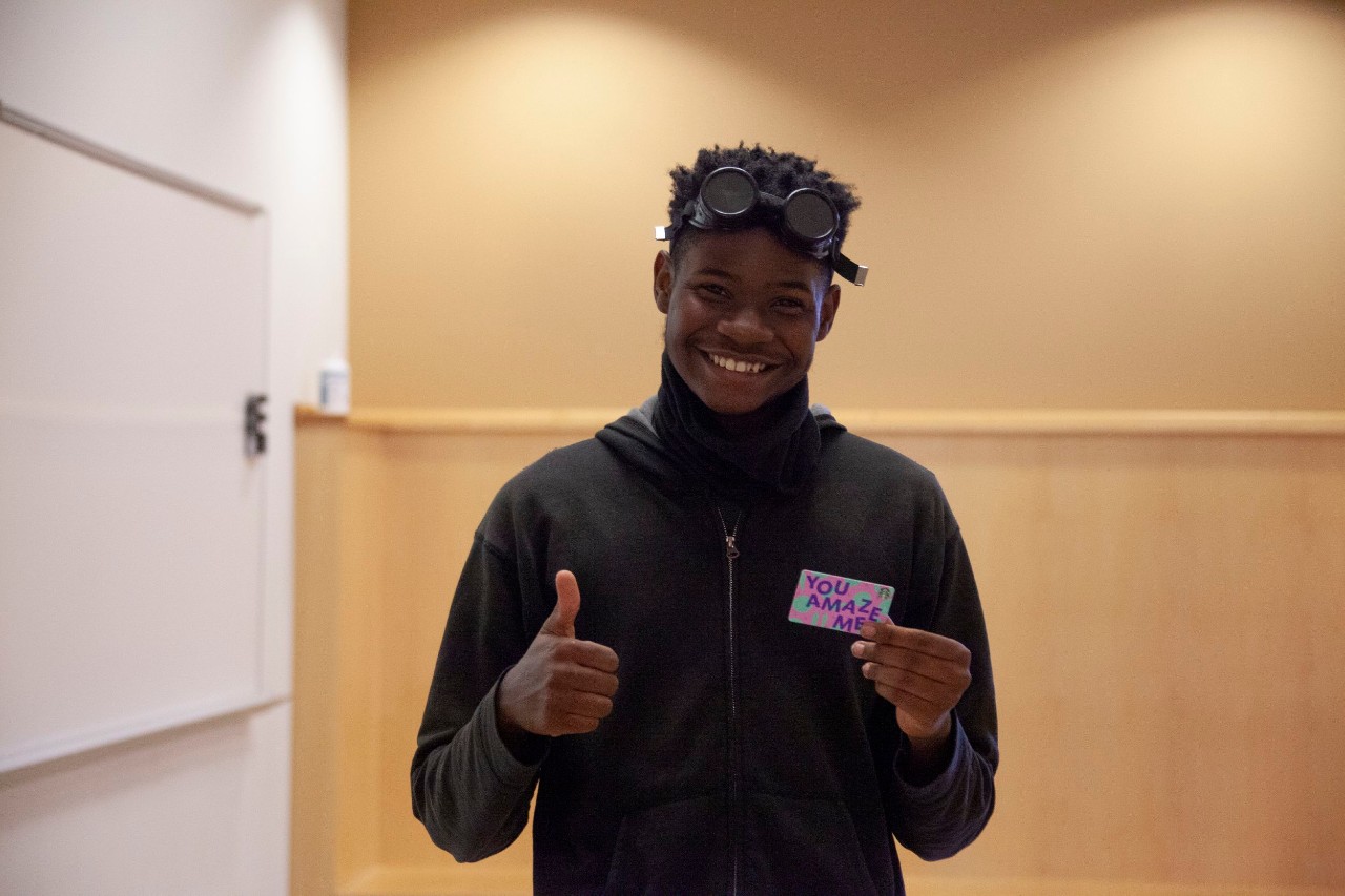A student holds up a gift card while flashing a thumbs up.
