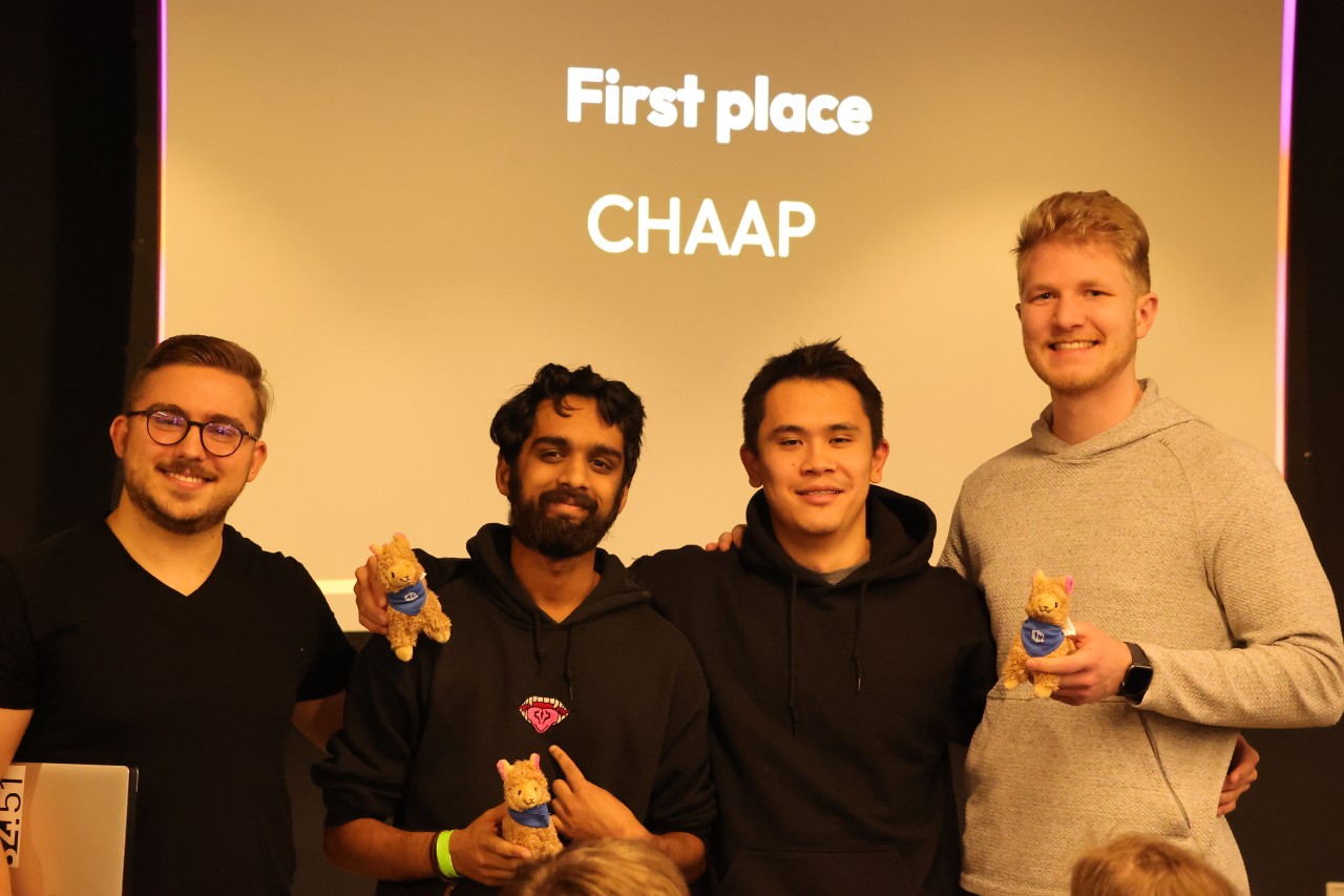 Four people stand in front of a screen that reads "first place."