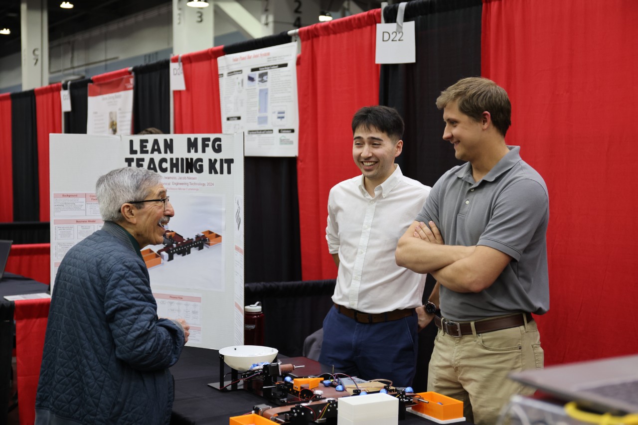Two students speak to a judge at the Expo, they all smile. 