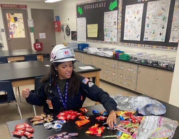 woman in hard hat sorts candy at a table in an elementary school classroom