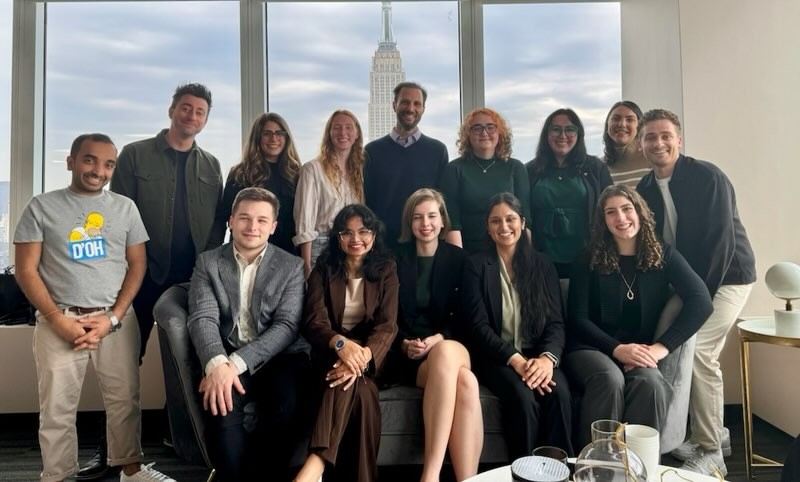 group of people posed before a large window with the Empire State Building in background
