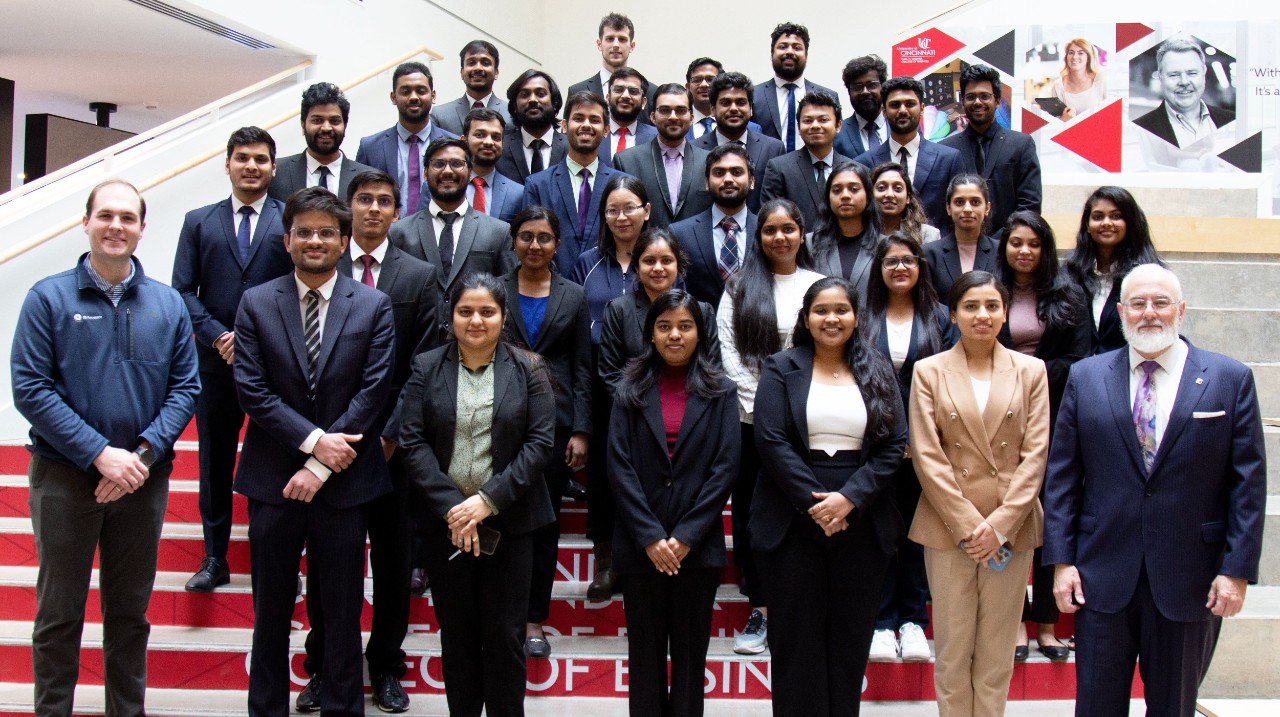 Students, faculty and an alumnus stand on the Lindner Hall atrium steps.