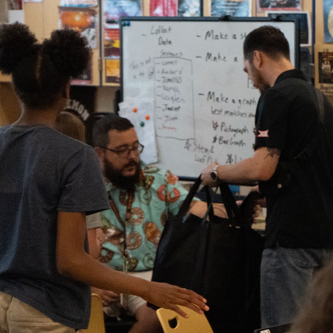 man hands black bag to teacher in a classroom