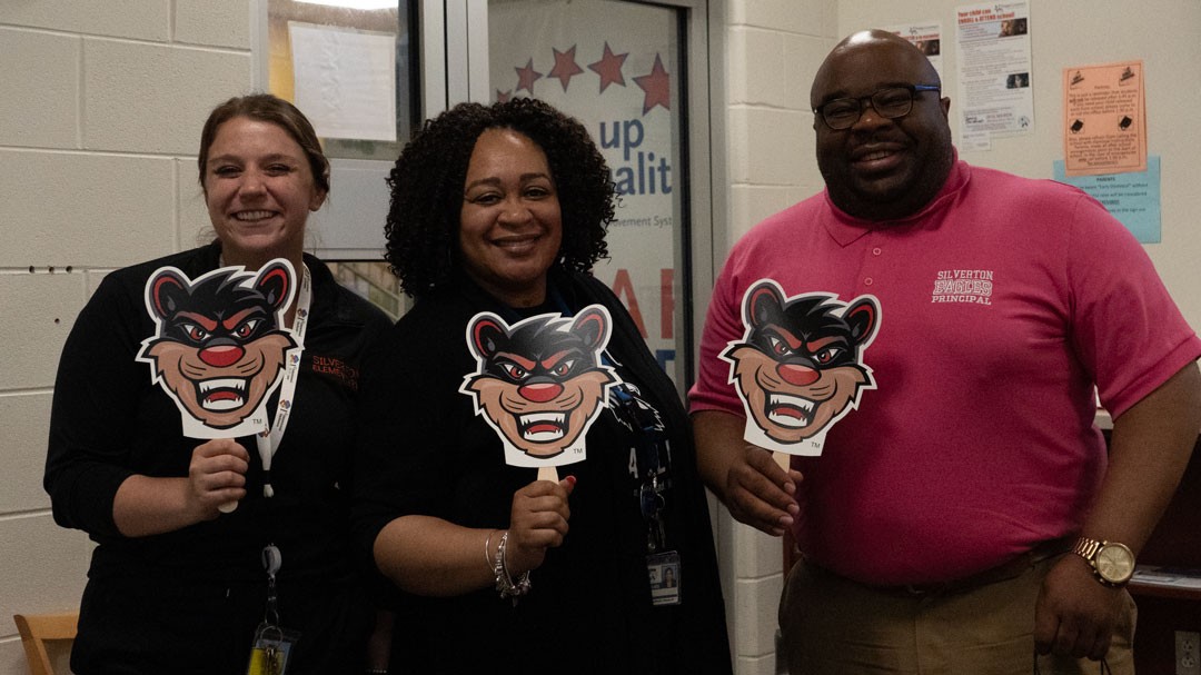Three people stand holding fans with a cartoon bearcat image on it.