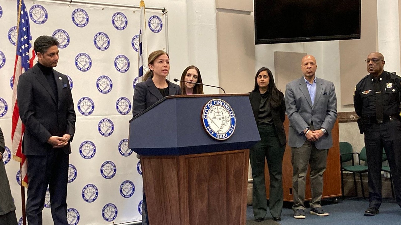 Dr. Amy Makley stands at a podium and speaks at a press conference with other leaders and city officials standing nearby