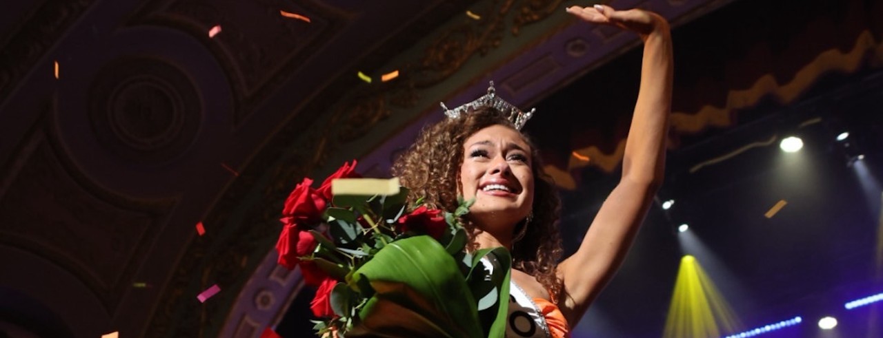 Stephanie Finoti holding a bouquet of flowers is covered in confetti as she waves to supporters on stage.