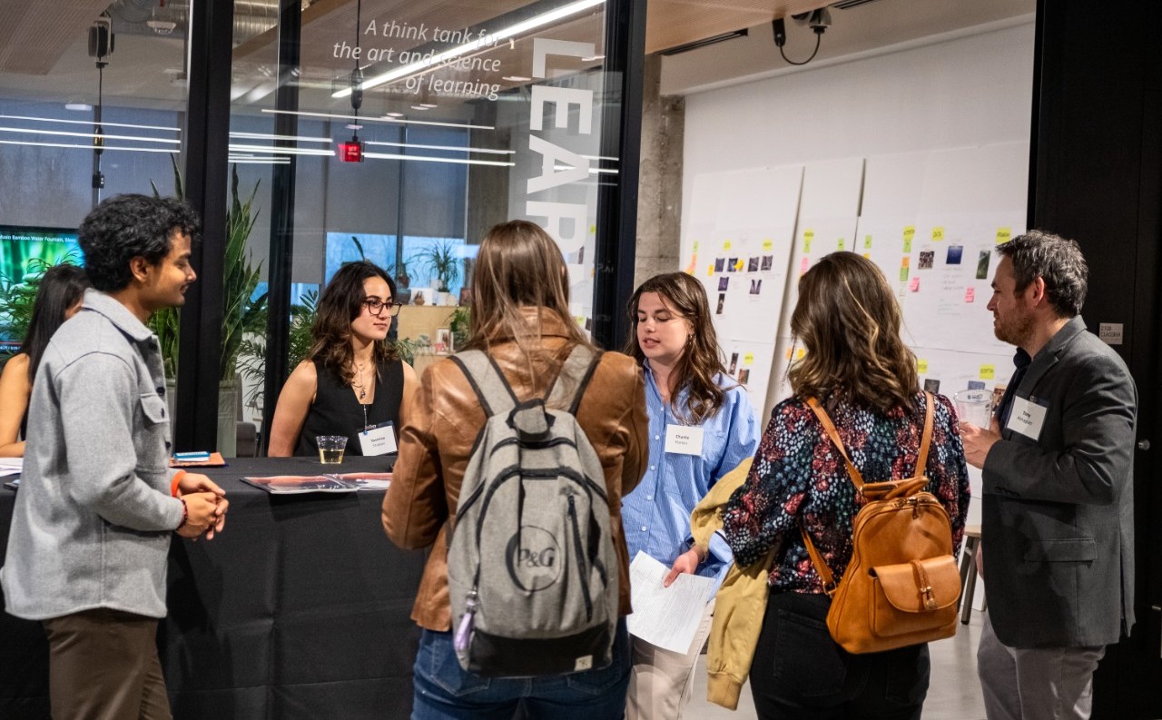 Six men and women wearing backpacks stand around a table in UC's 1819 Innovation Hub.