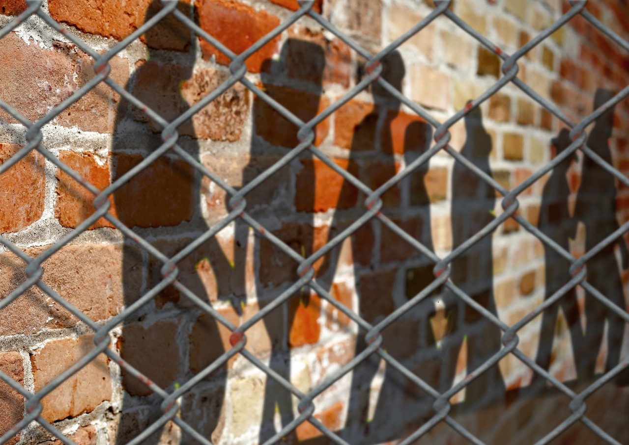 brick wall with shadows of people and a fence wire on top