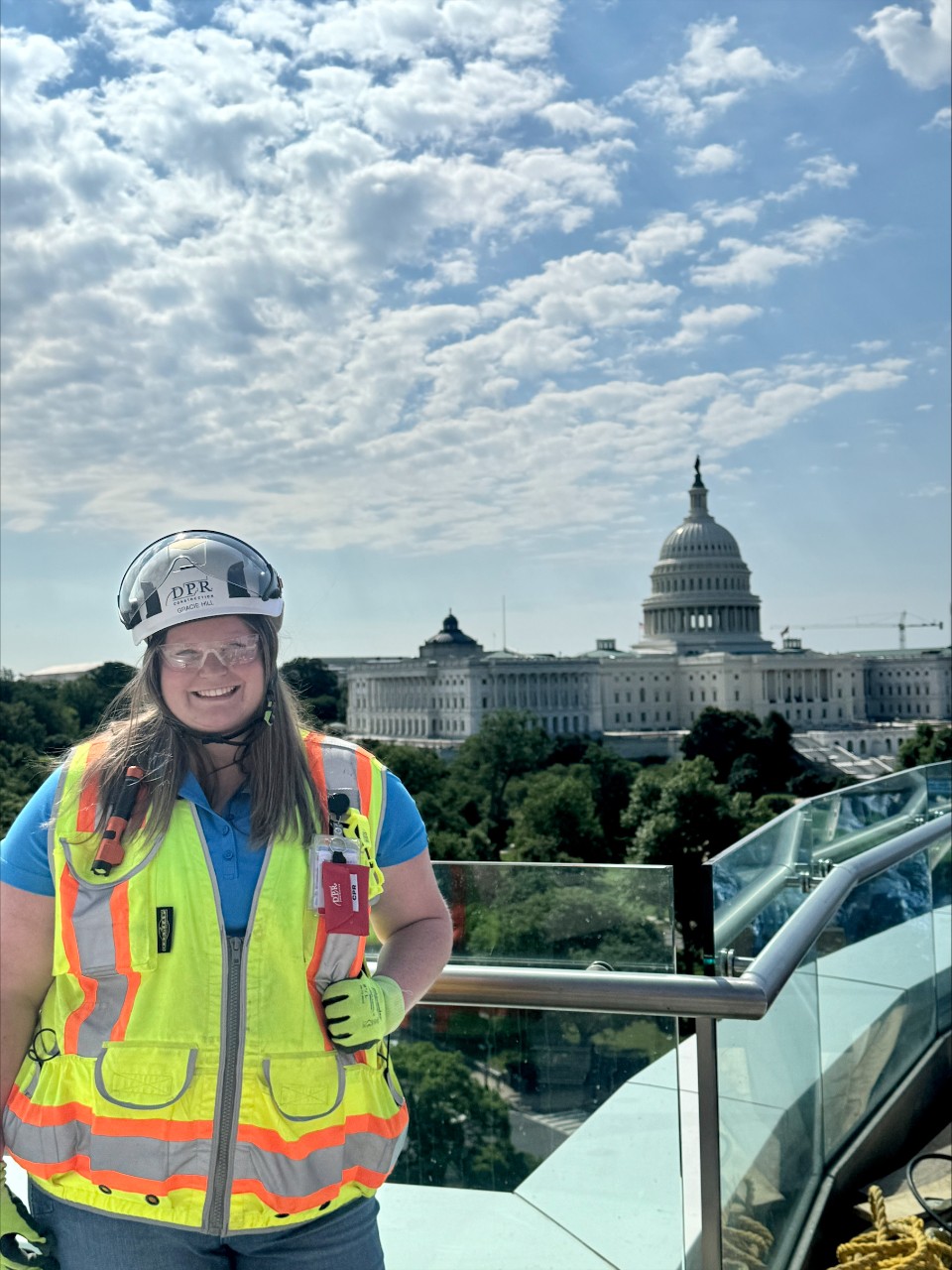 A woman in a safety vest and hard had poses on a building in front of the US capitol