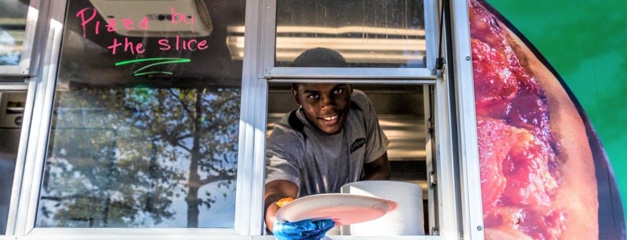Person wearing gray shirt handing pizza slice from food truck window