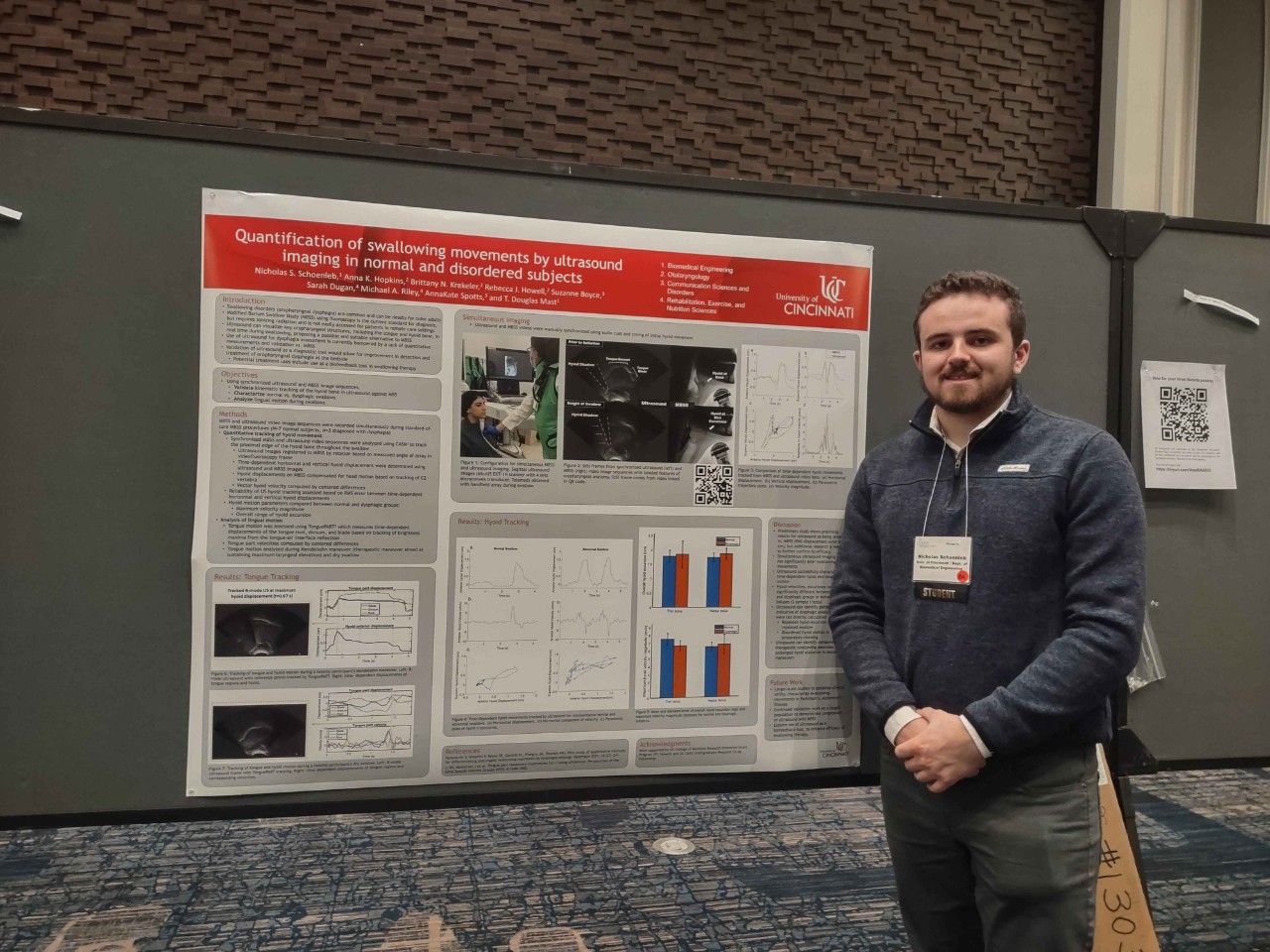 A man stands next to a research poster at a conference 