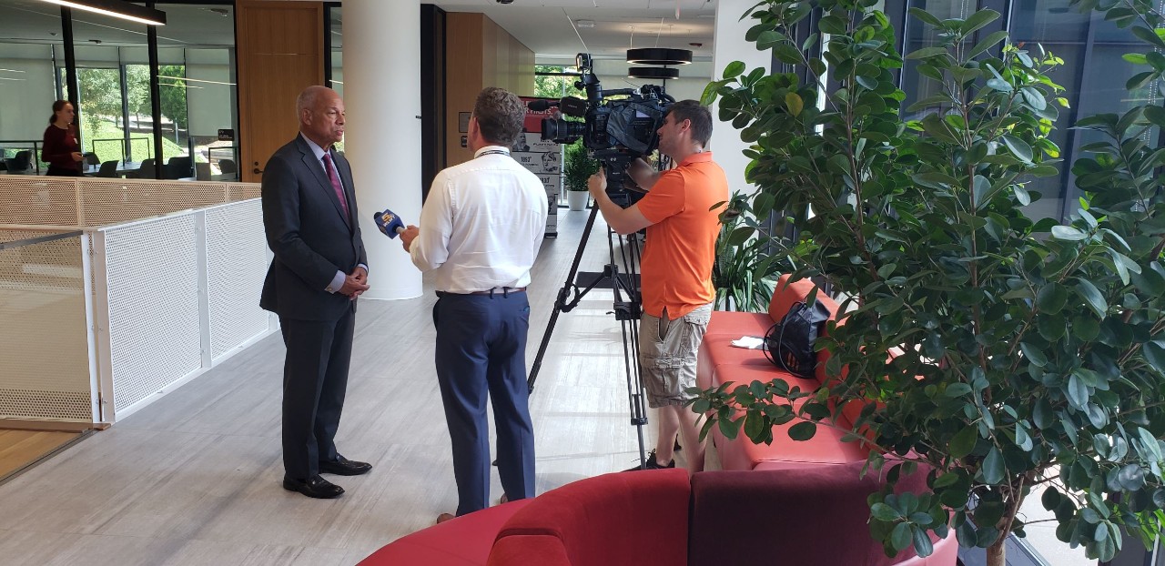 Jeh Johnson shown in UC Law atrium with a TV camera pointed his way and two journalists asking questions