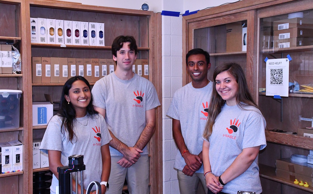 Four people in matching T-shirts pose for a photo in front of cabinets featuring examples of 3D prosthetics.