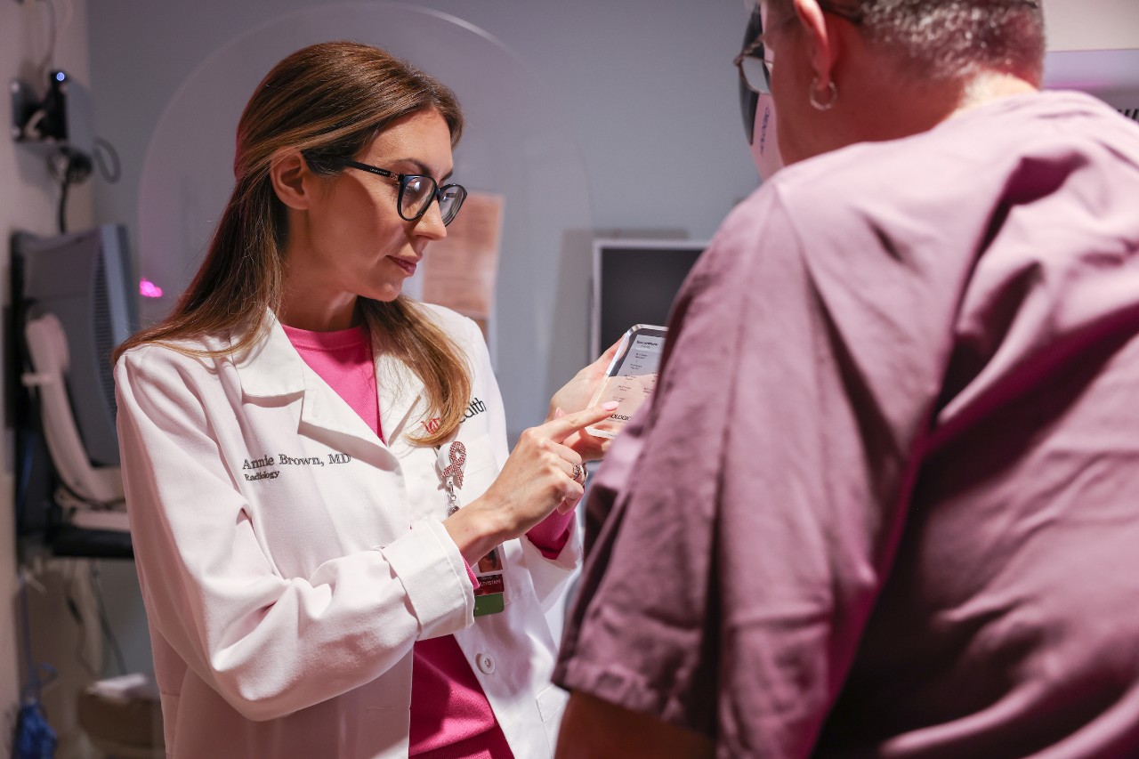 Ann Brown, wearing a white lab coat, points at a tablet she is holding while speaking with a patient