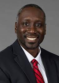 A smiling photo of James Mack with a red triped tie and suit jacket.