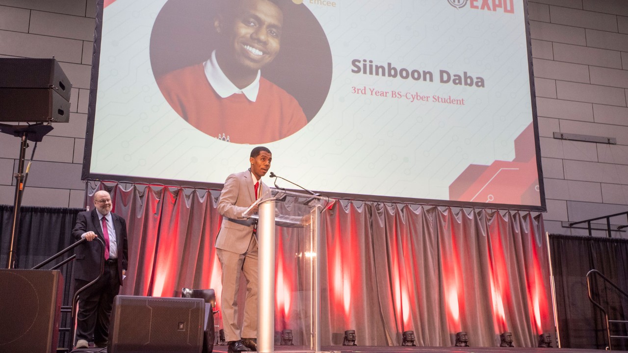 Siinboon Daba, wearing a tan suit, speaks to a roomful of people at the 2024 IT Expo