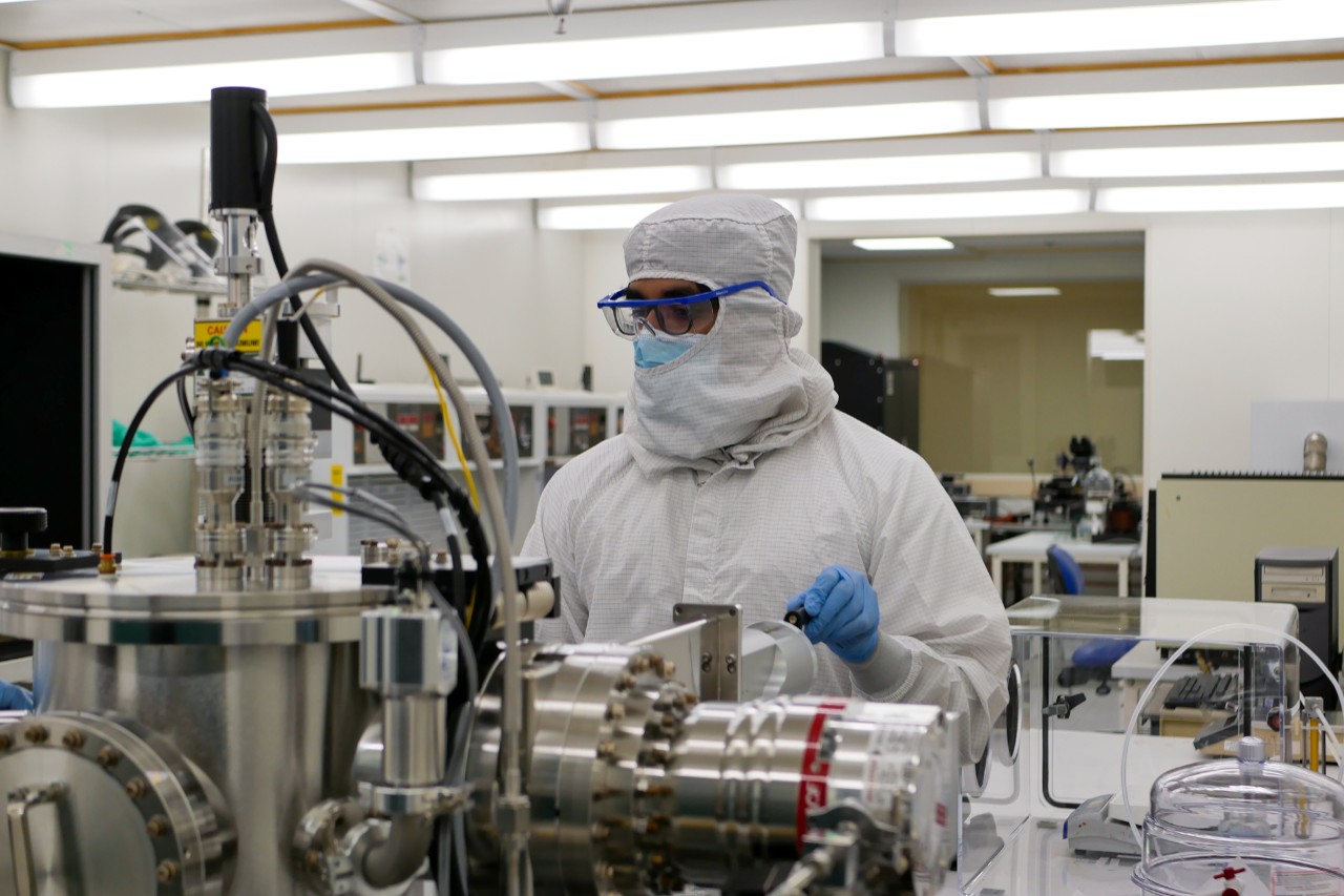 student in white protective clothing works on equipment in cleanroom