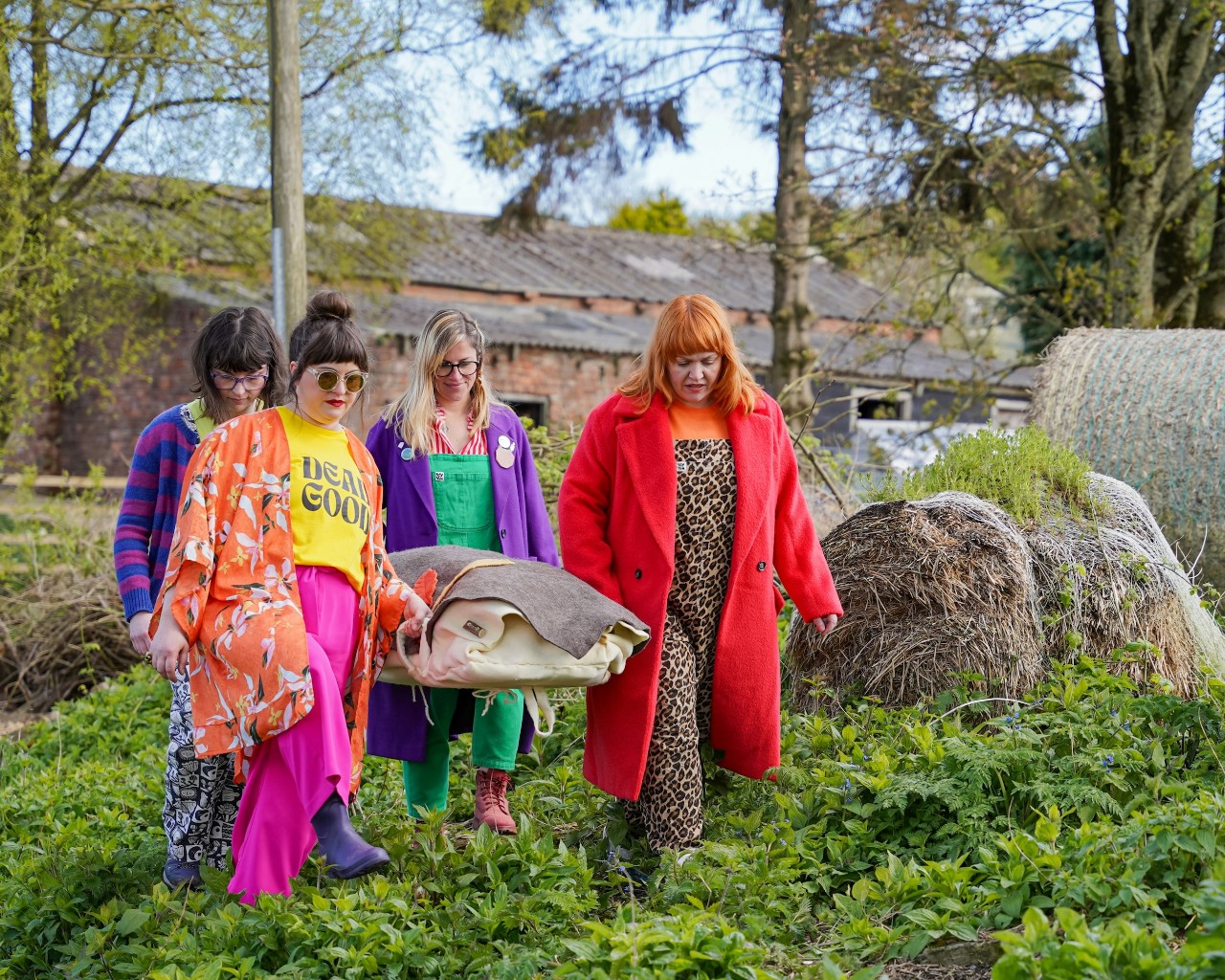 Four friends in bright clothing carrying a woollen felt shroud in a woodland burial setting