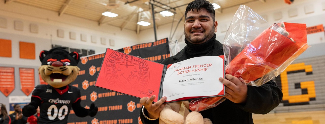The Bearcat Mascot stands near Harsh Minhas as he holds a certificate showing he is a Marian Spencer Scholarship winner