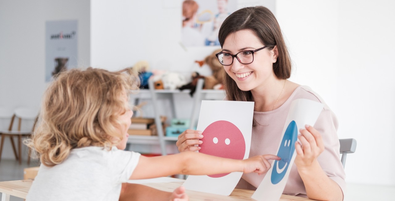 small child pointing to a happy face on a piece of paper.