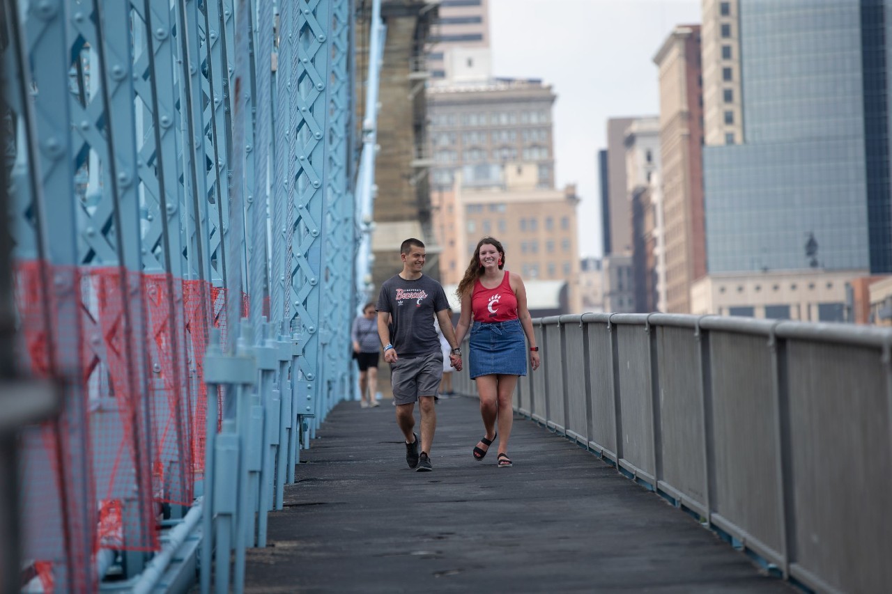 Young man and woman dressed in UC swag walk across a bridge in Cincinnati