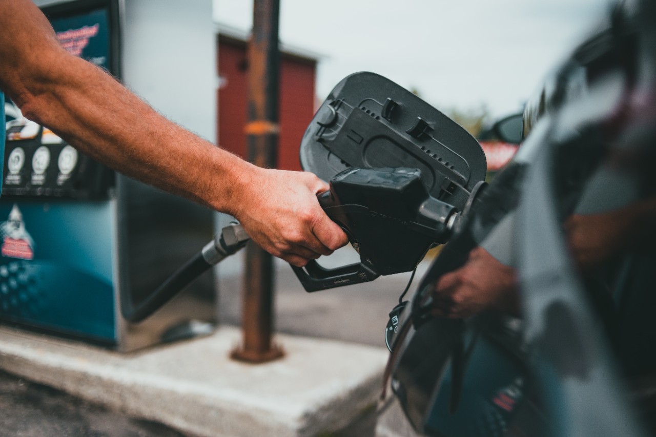 A hand holds a gas nozzle while filling a car's tank.