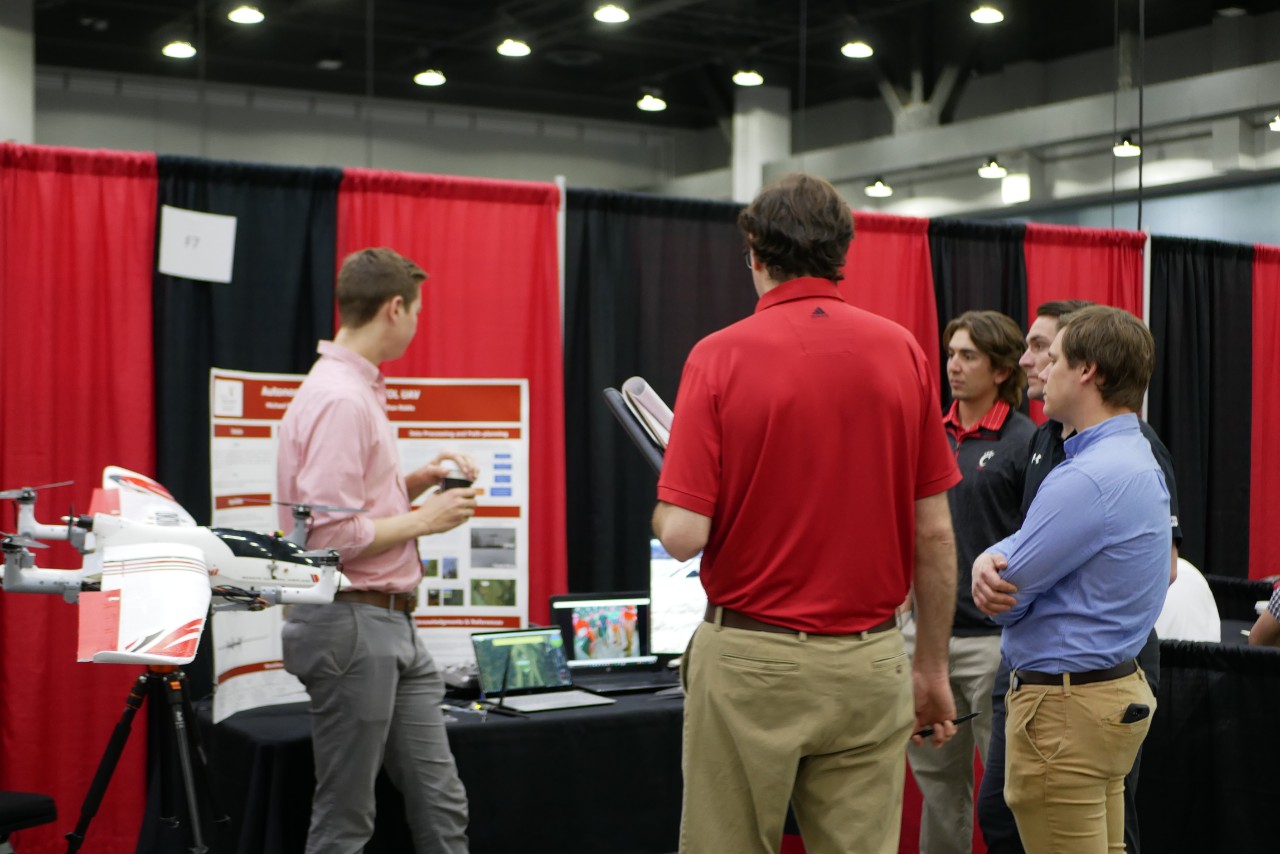 students stand around their booth at the CEAS Expo. Next to them, is their project, a model aircraft. 