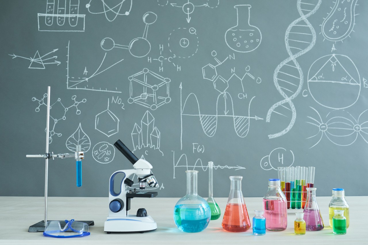 Illustration of educational lab environment with drawings on chalkboard and colorful liquids in test tubes and microscope. 