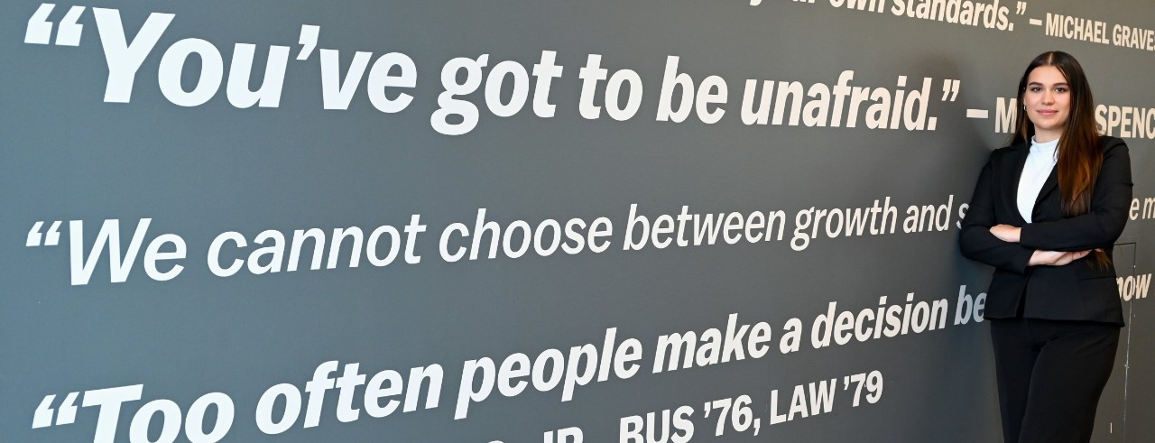 Mirsayah Wasnuk stands in a black suit and in front of a wall of quotes.