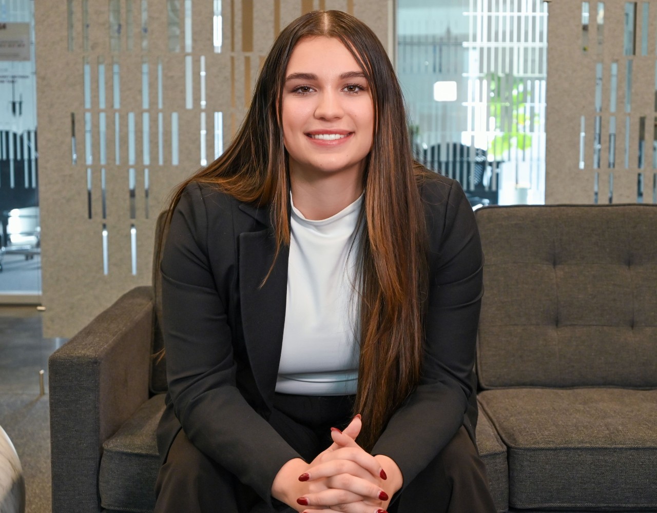 Mirsayah Wasnuk sits on a dark couch in a black suit and looks into the camera.