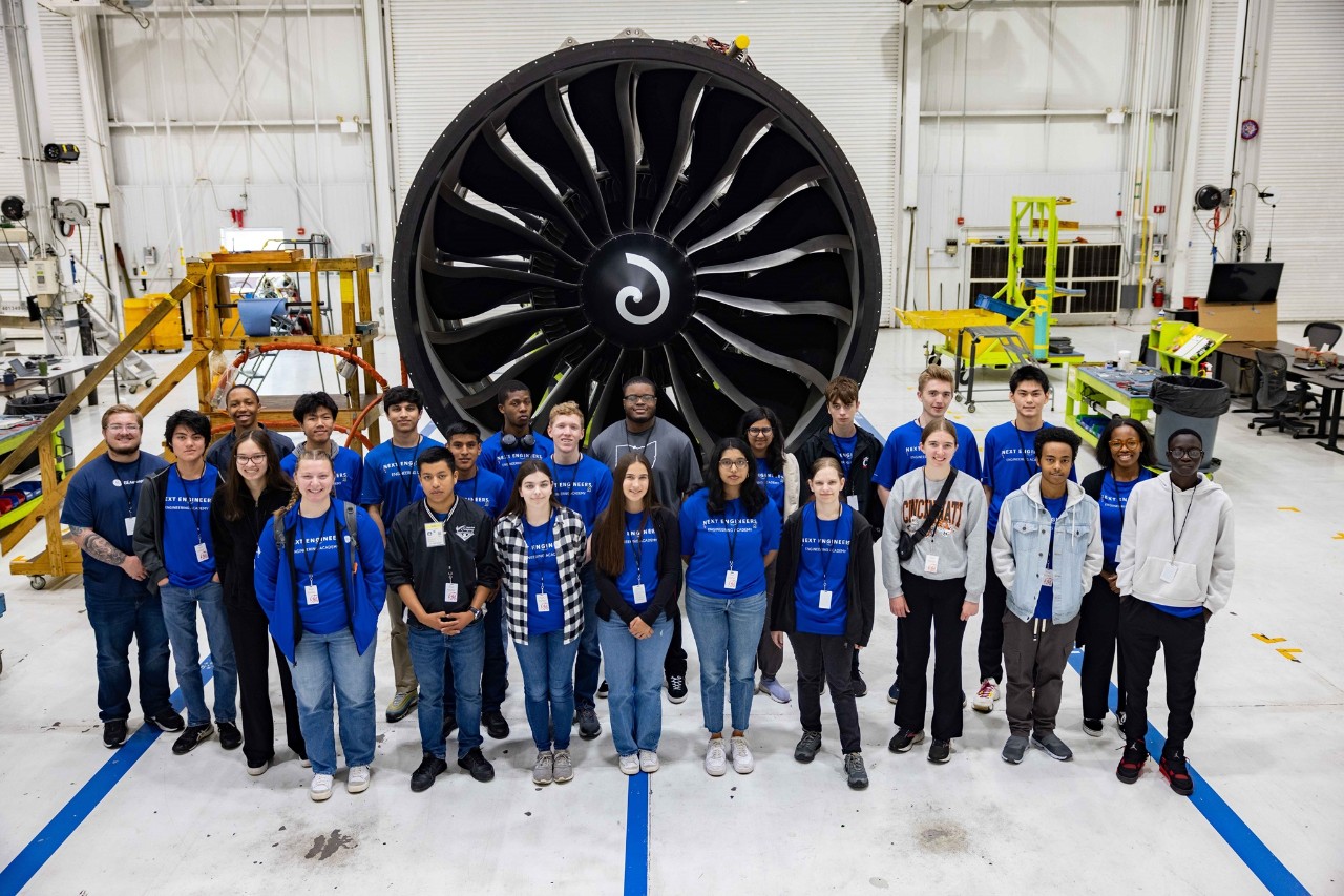 High school students stand in front of an enormous jet engine in the Evendale plant.