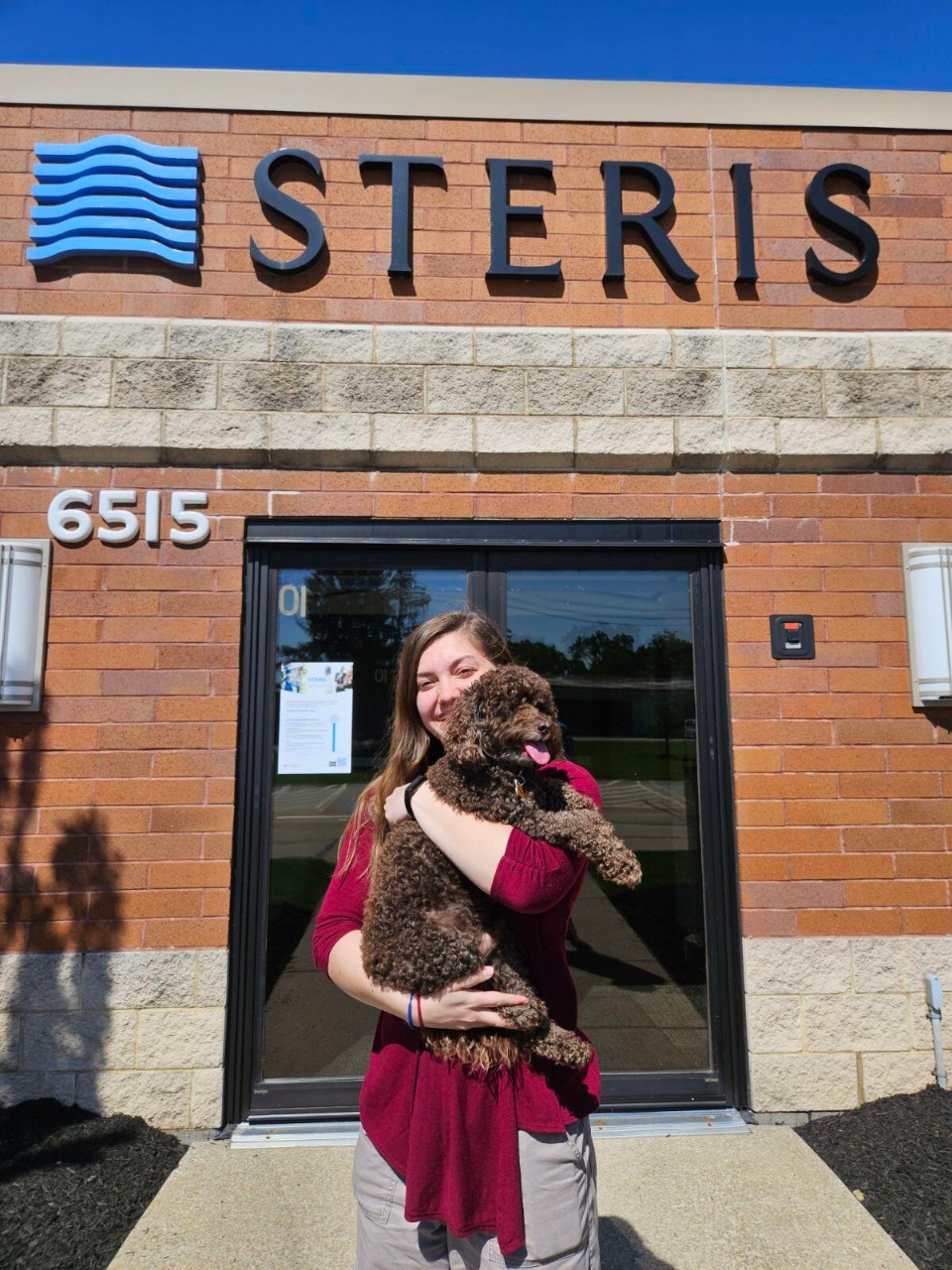 Teresa Hawk stands outside of STERIS and holds a small, brown dog. 