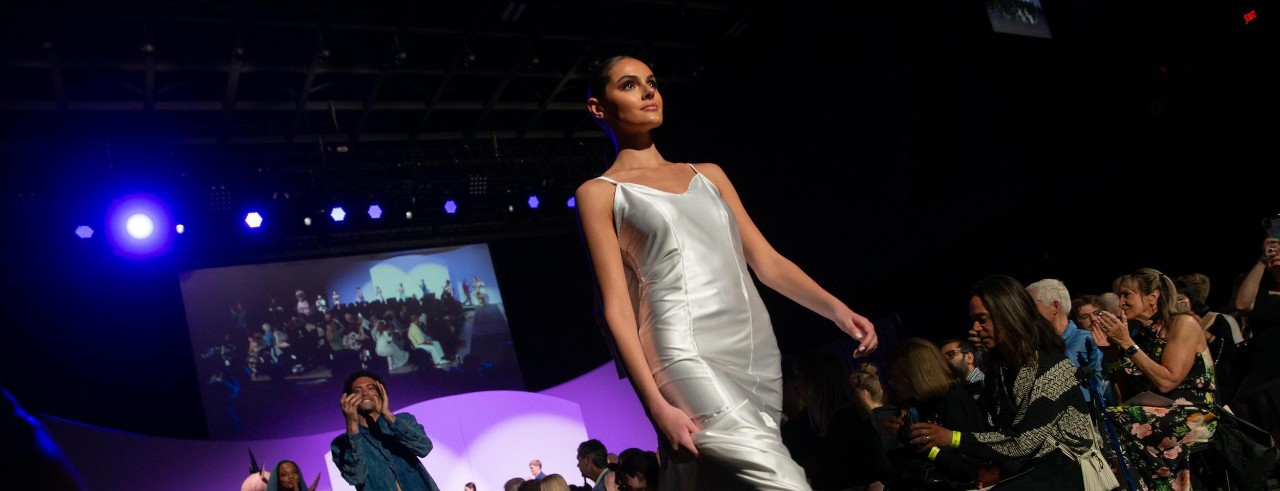 Female in long ruffled dress on the runway with lights and an audience