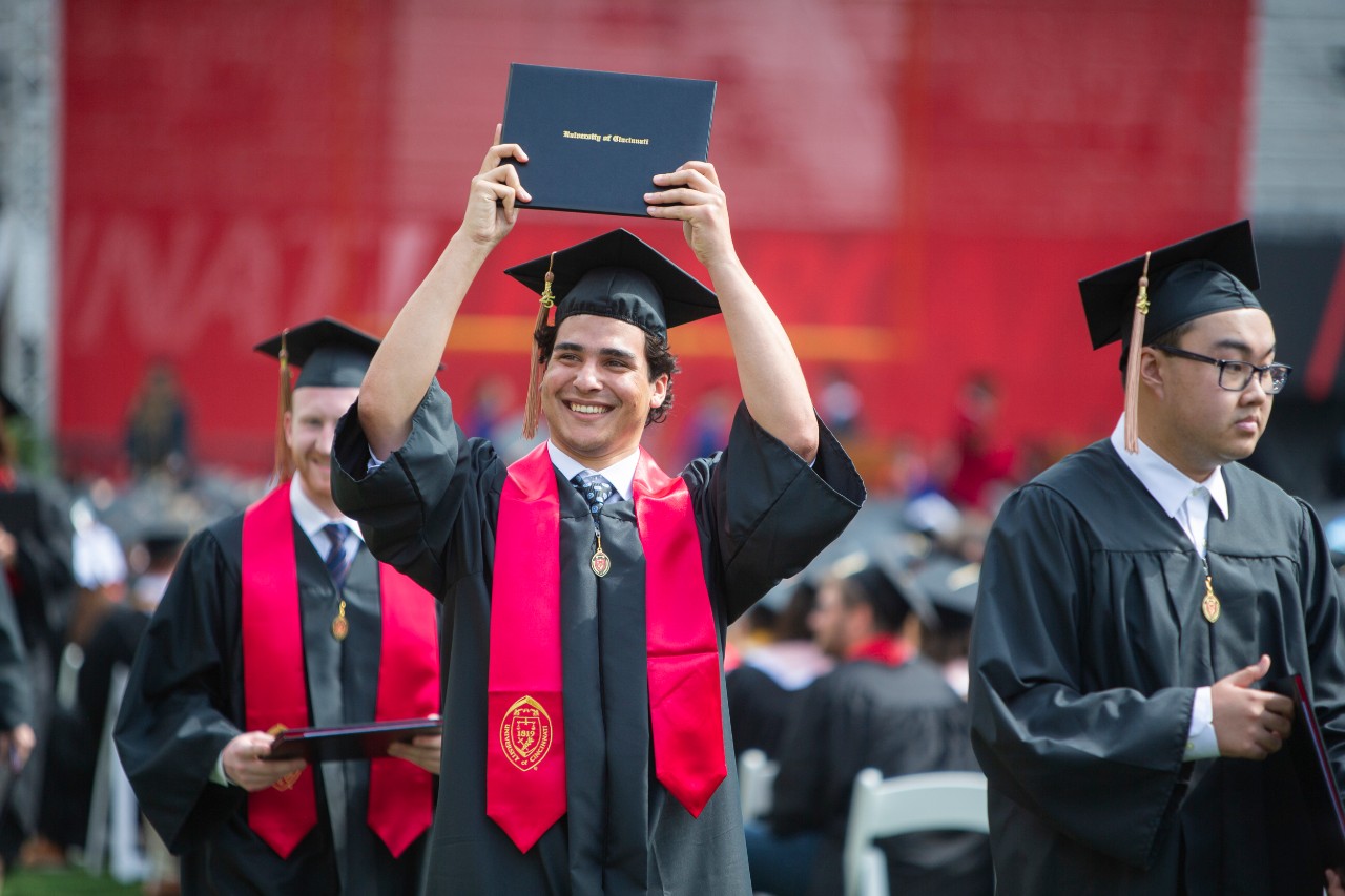 A graduate holds up his diploma at Nippert Stadium.