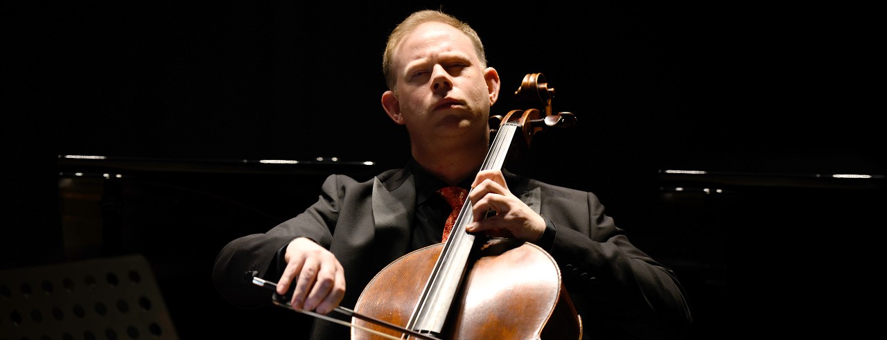 A performance photo of cellist Benjamin Hughes. 