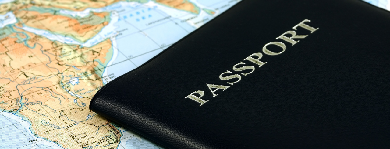 Stock image of a world map with a black passport booklet laying on top of it. 