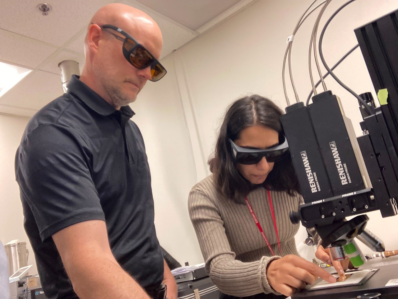 Two people in protective glasses prepare a slide under optical equipment.