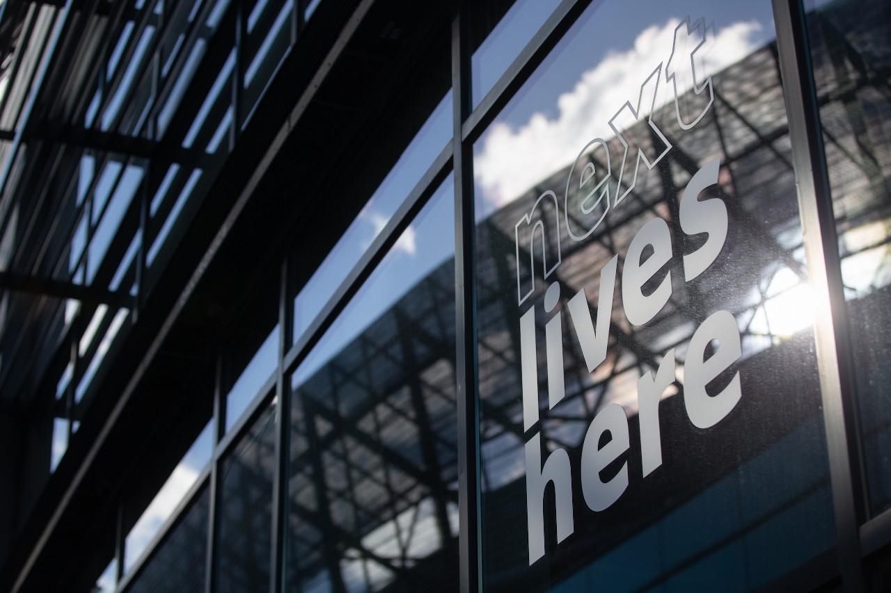 Next Lives Here reflection in building window on campus at the University of Cincinnati